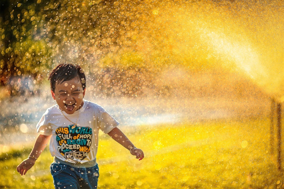image of young child laughing and running through a sprinkler